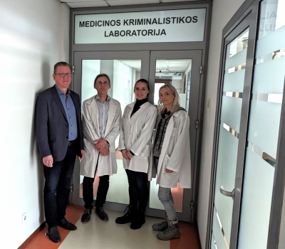 Četri cilvēki stāv pie durvīm virs kurām ir uzraksts Medicinos kriminalistikos laboratorija