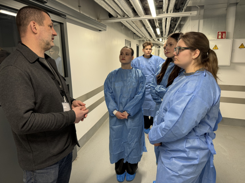 Vīrietis stāsta un jaunieši zilos halātos stāv un klausās