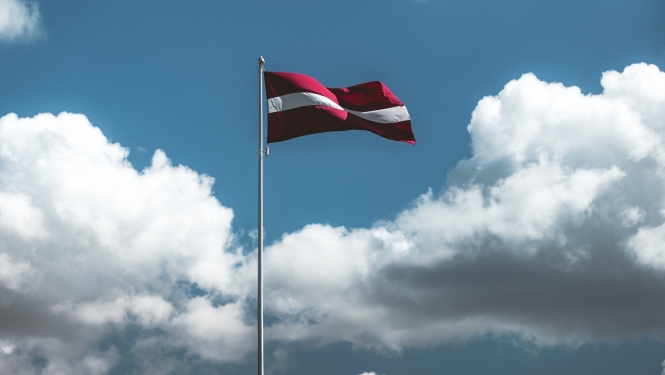 Latvijas karogs mastā uz debesu fona