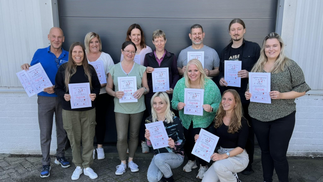 Divpadsmit cilvēku grupa pozē ar sertifikātiem rokās