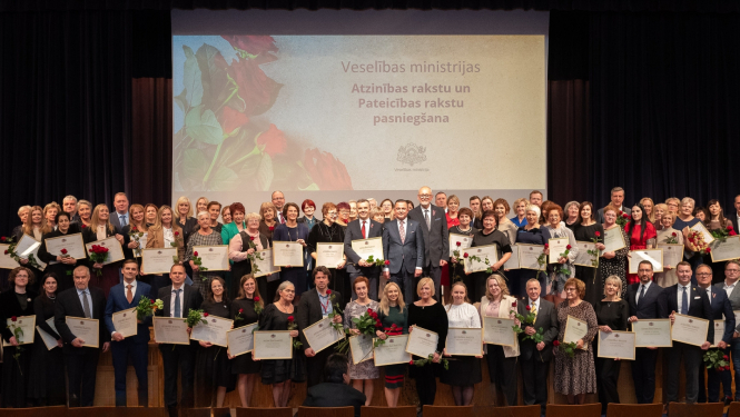 Liels daudzums cilvēku sastājušies vairākās rindās koppbildei, tiem rokās ir ierāmētas atzinības un pateicības raksti