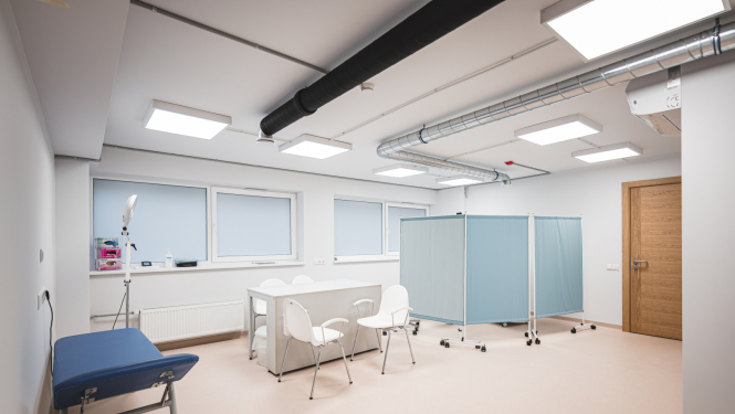 Balta telpa, kurā atrodas zila kušete, galds un divi krēsli un gaiši zils aizlietnis