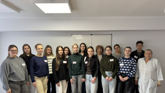 Vairāki cilvēki stāv pie baltas sienas un pozē fotogrāfam