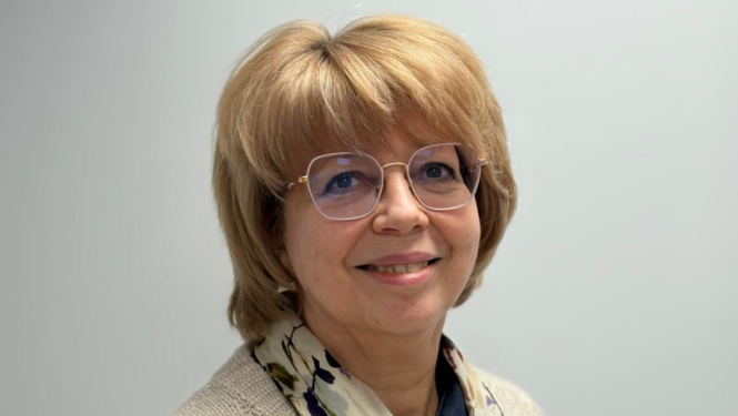 Sieviete stāv un smaida, balta siena fonā