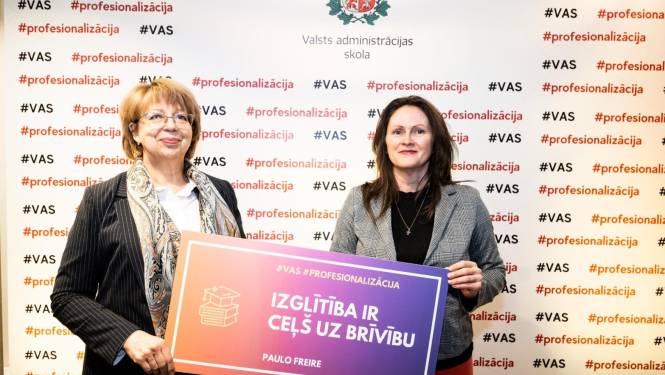 Divas sievietes stāv ar muguru pret sienu, uz kura ģērbonis un uzraksts Valsts administrācijas skola, abas rokā tur plakātu ar uzrakstu - Izglītība ir ceļš uz brīvību