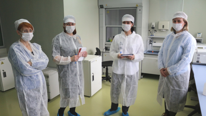 Četras sievietes baltos halātos un ar maskām uz sejas stāv laboratorijas telpās