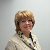 Sieviete stāv un smaida, balta siena fonā