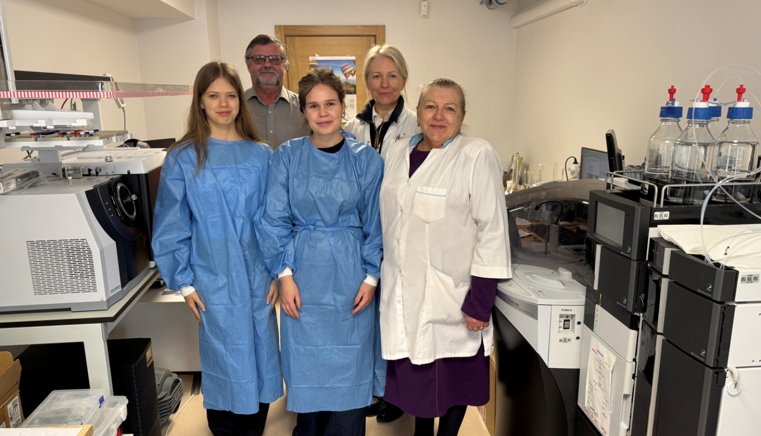 Pieci laboratorijas darbinieki halātos atrodas laboratorijas telpās