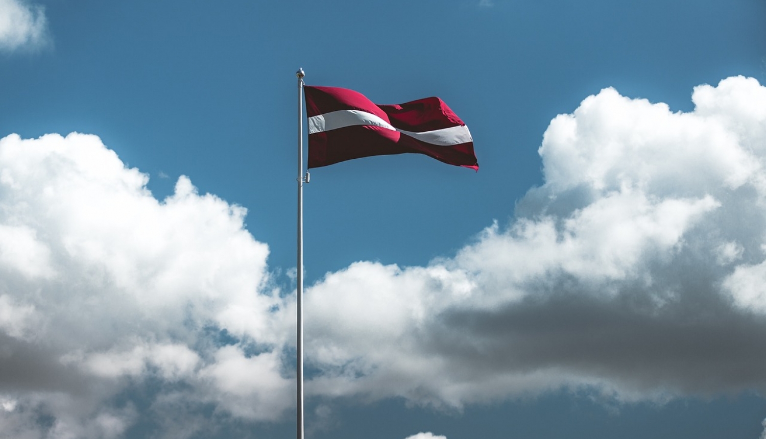 Latvijas karogs ar debesīm un mākoņiem fonā